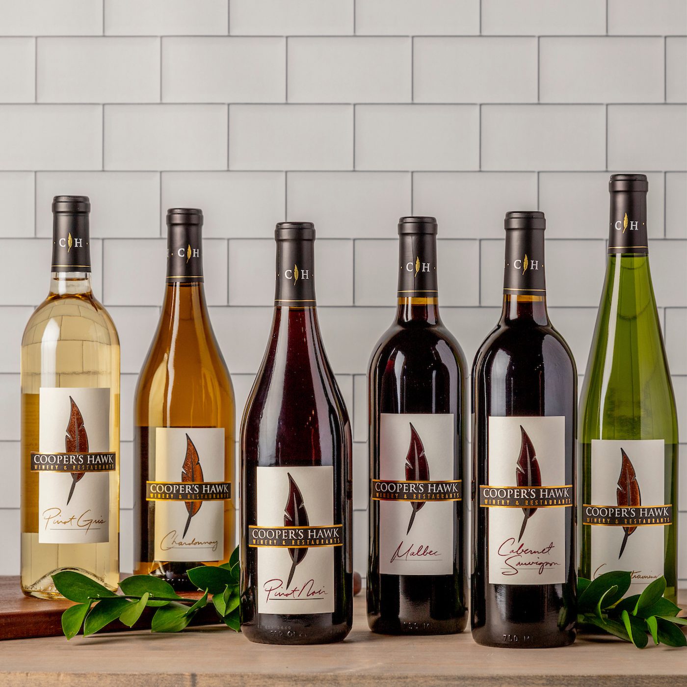 Six Cooper's Hawk wine bottles with assorted labels: Pinot Grigio, Chardonnay, Pinot Noir, Malbec, Cabernet.