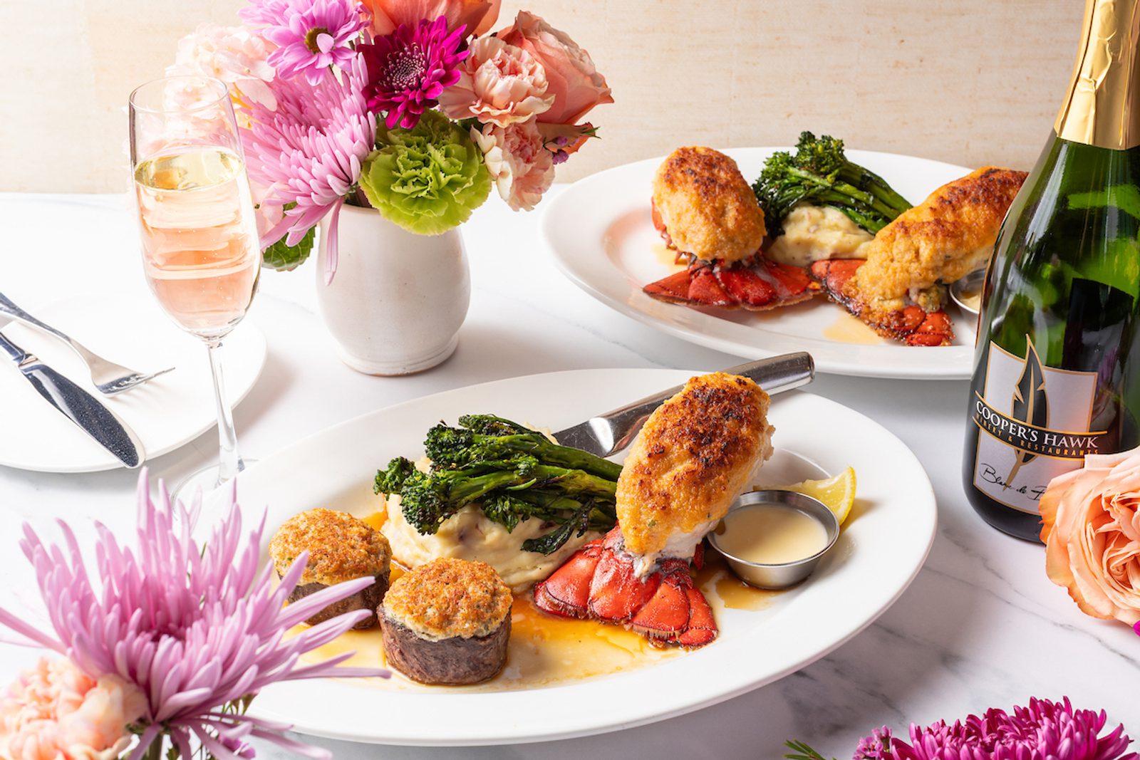 Lobster tails topped with crab stuffing on mashed potatoes, broccolini, dipping sauce, and a glass of champagne