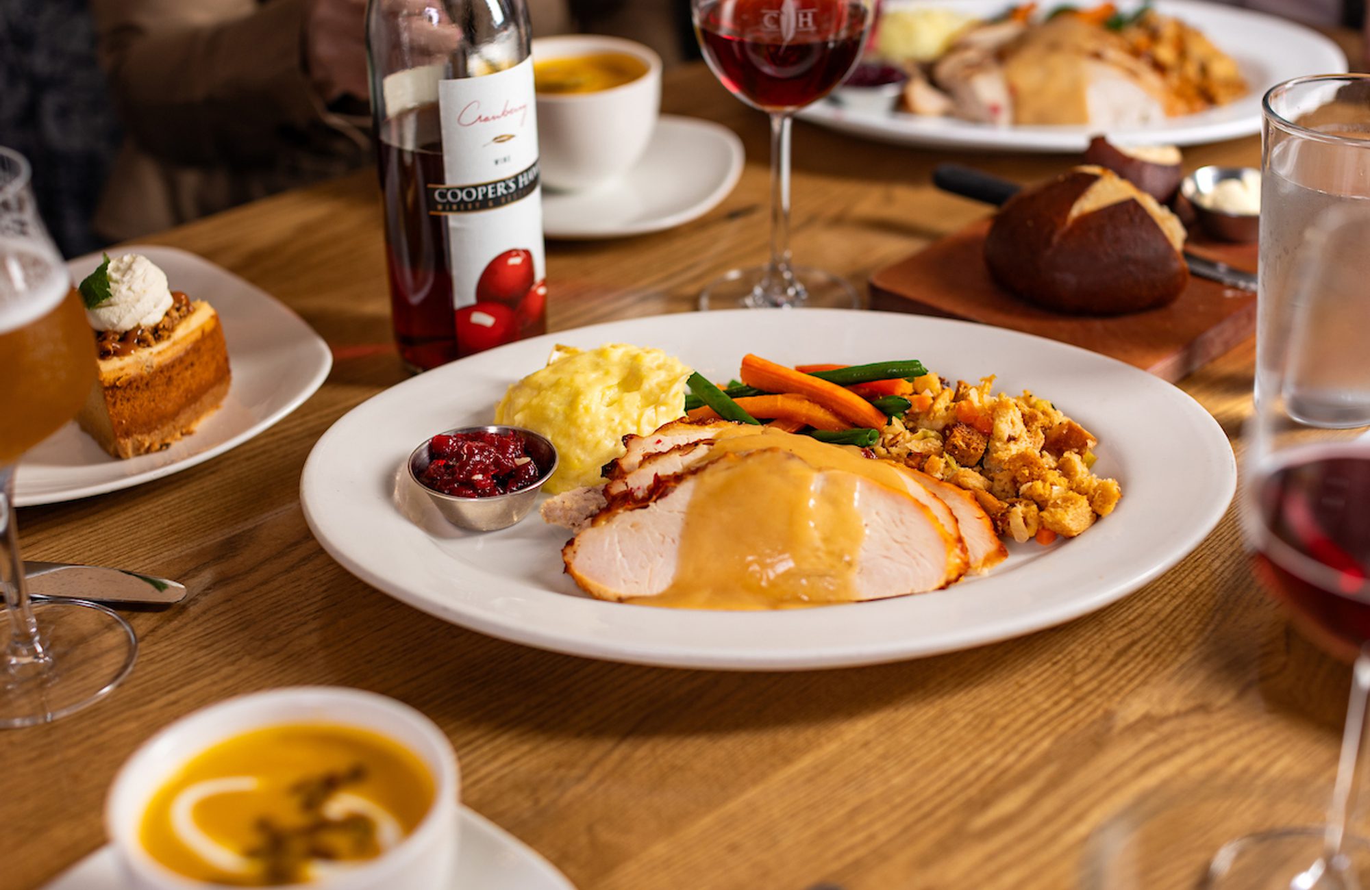 Roast turkey dinner with mashed potatoes, vegetables, stuffing and cranberry sauce on a table with wine, bread, soup, and dessert plates