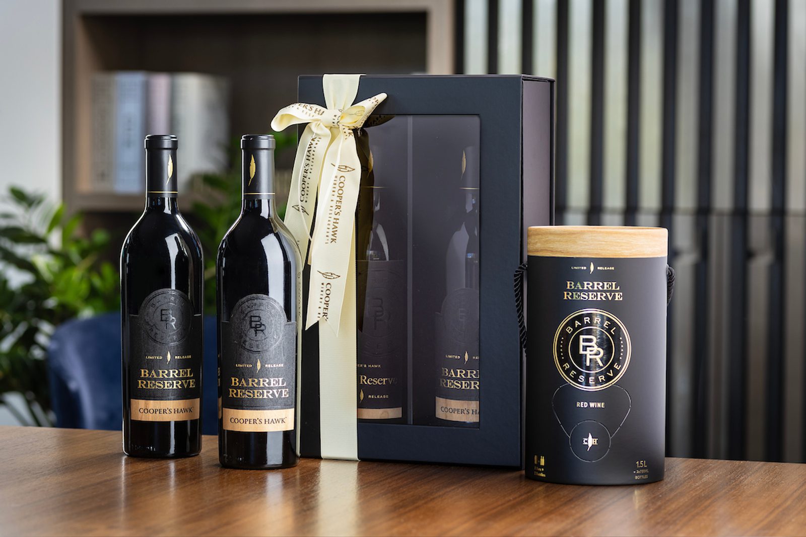 Two bottles of Barrel Reserve red wine, a boxed gift set tied with a ribbon, and a Barrel Reserve cylindrical container on a table.