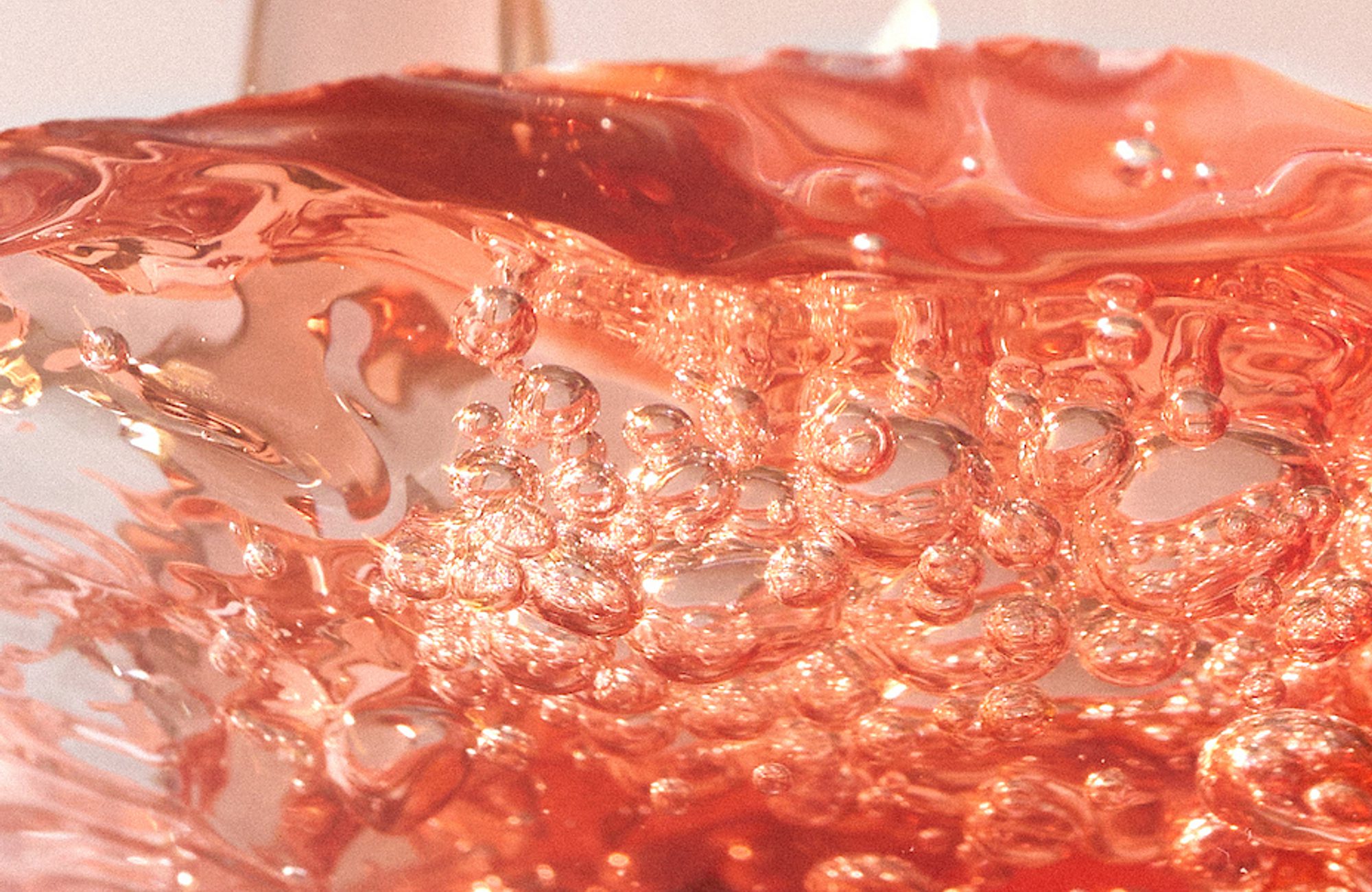 Pinkish-red liquid being poured, showing bubbles and rippling surface
