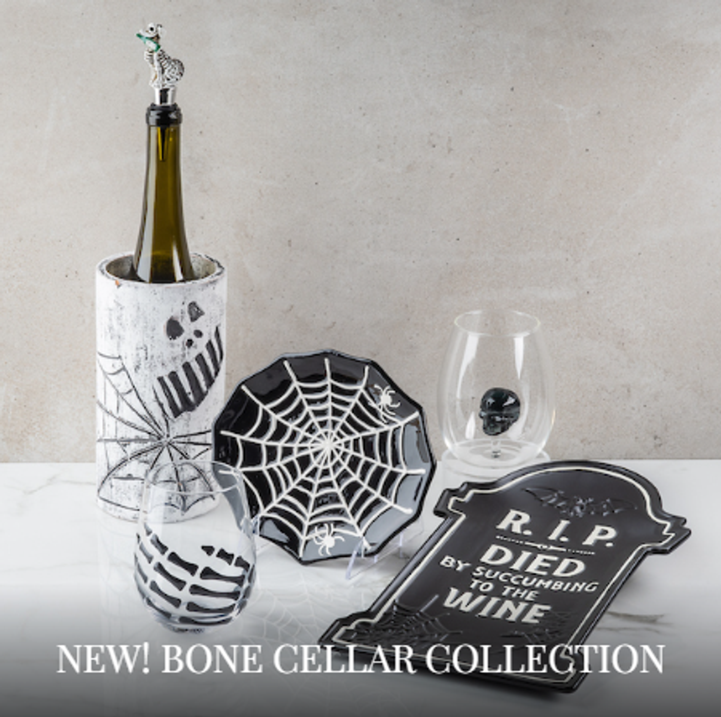 Halloween bone cellar collection display with a bottle in a skull sleeve, spiderweb plate, skull glasses, and a RIP tombstone sign on a white surface