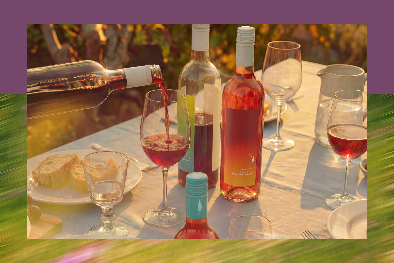 Wine being poured into a glass on an outdoor dining table with rosé bottles, wine glasses, bread and a water pitcher.