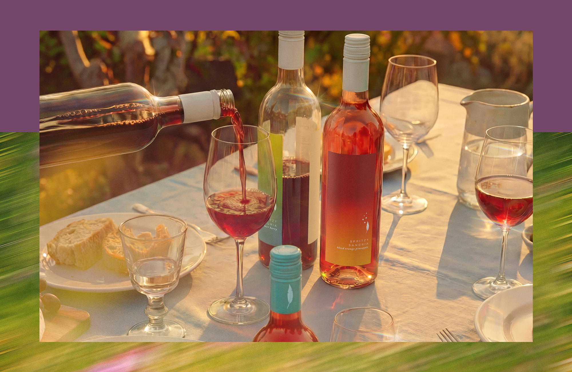 Wine being poured into a glass on an outdoor dining table with rosé bottles, wine glasses, bread and a water pitcher.