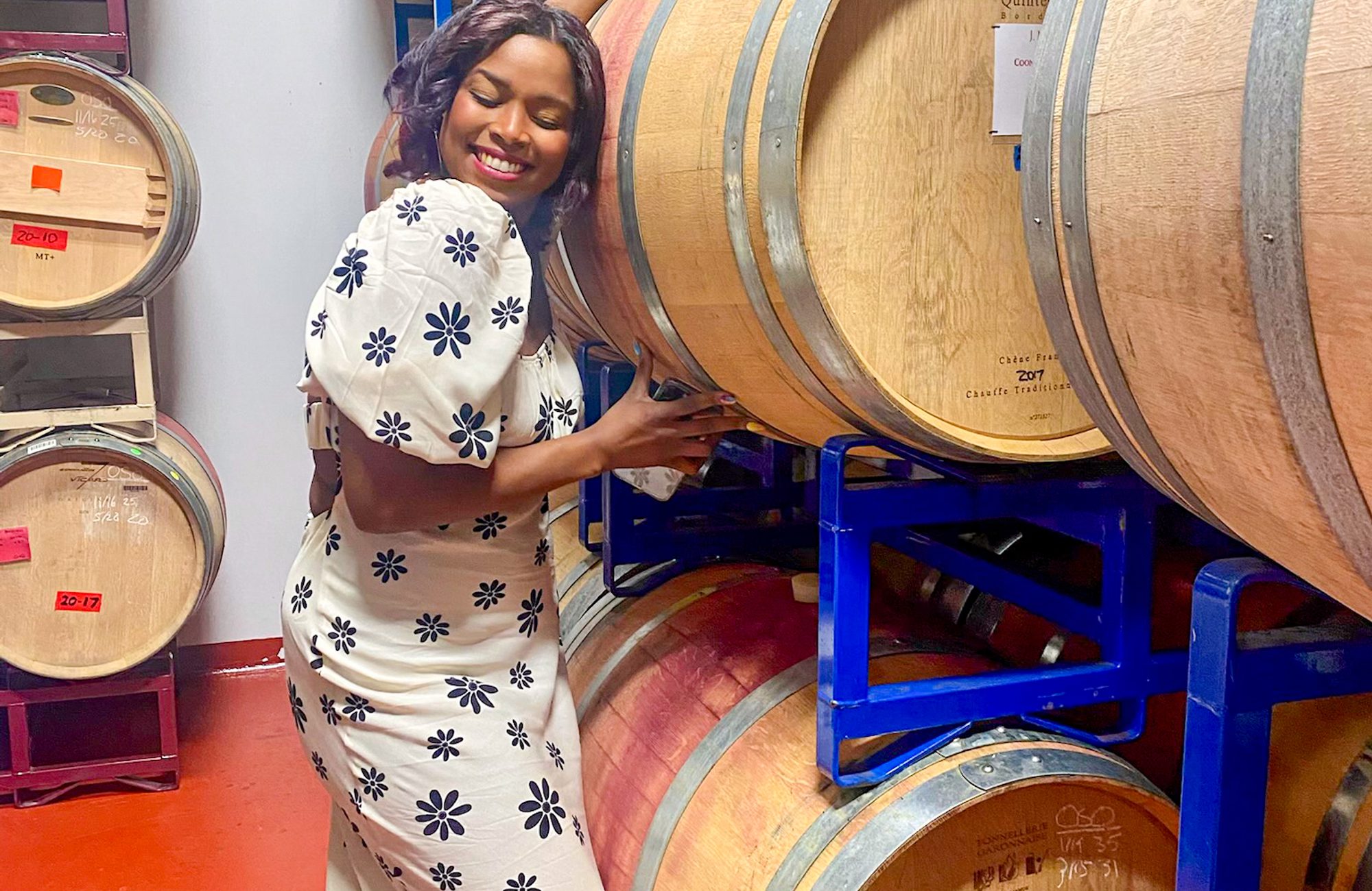 A woman in a dress standing next to a stack of barrels.