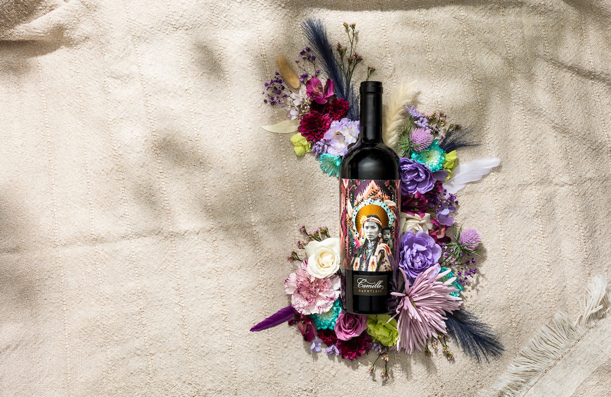 Camille Dauntless wine bottle with illustrated portrait label among purple, pink, and white flowers on beige cloth