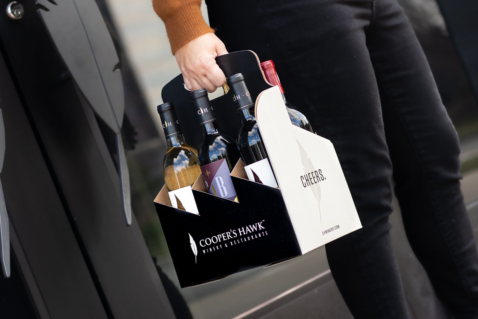 A woman is holding a box of wine in front of a building.
