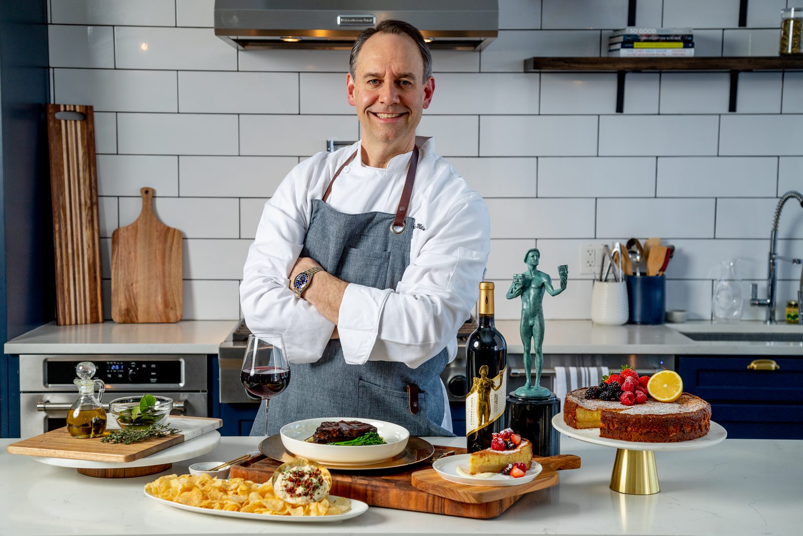 A man in an apron standing in front of a kitchen full of food.
