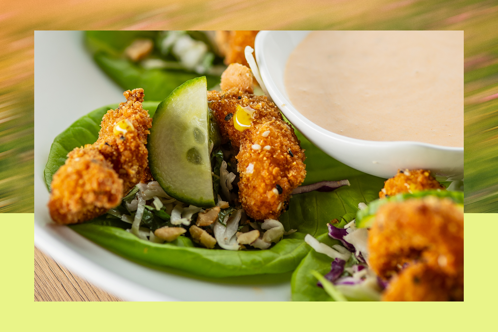 Breaded chicken bites on lettuce with a cucumber slice, shredded cabbage and chopped nuts, and a bowl of creamy dipping sauce.