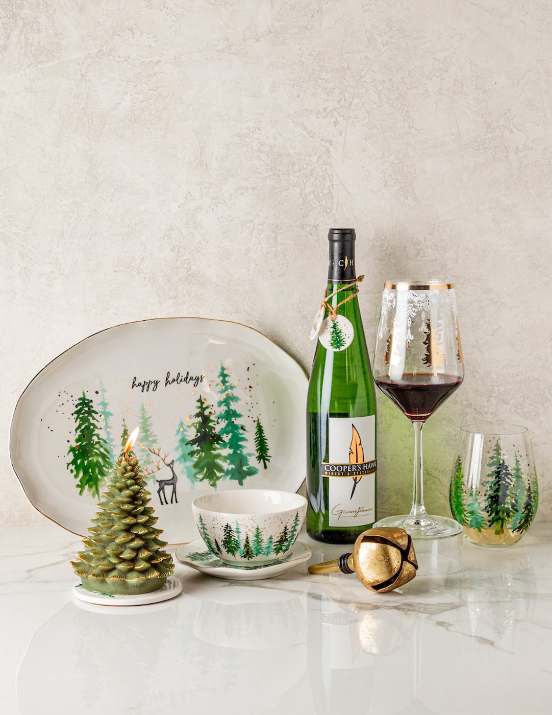 Holiday table setting with happy holidays platter (evergreens, deer), lit pine-tree candle, Cooper's Hawk wine and glasses