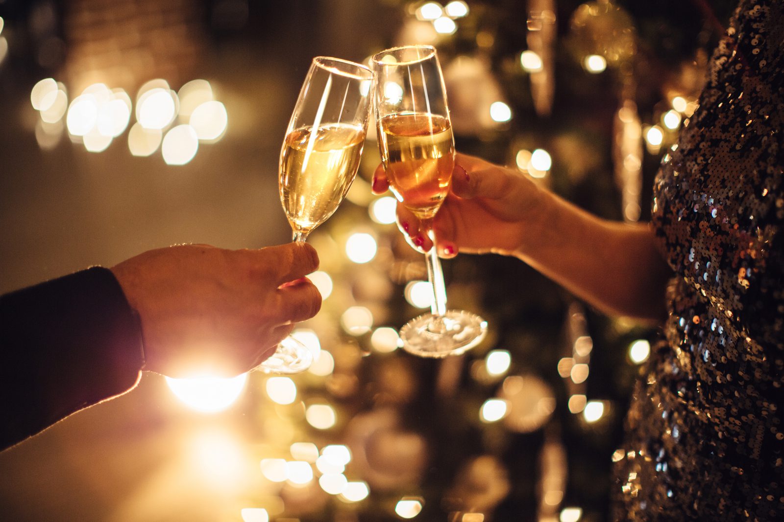 Two people clinking champagne flutes at a festive gathering with blurred warm lights in the background