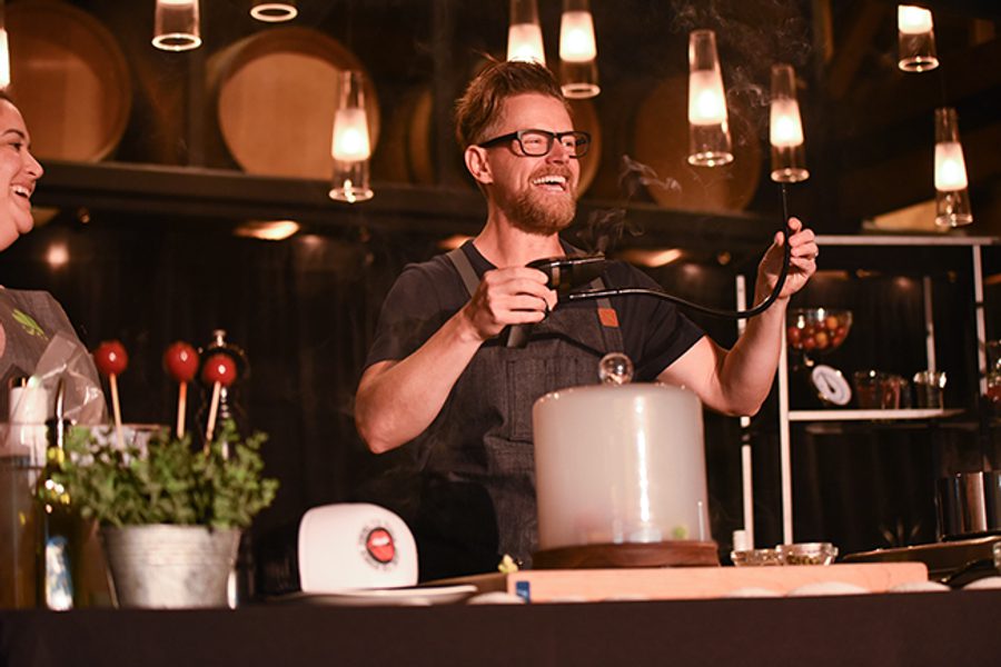 Two men standing in front of a table with a bottle of wine.