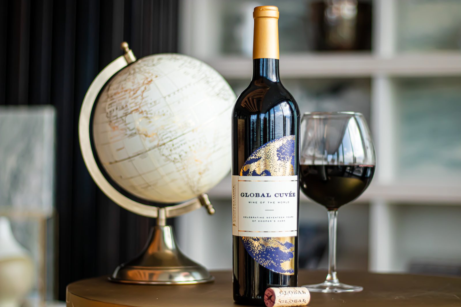 A bottle of wine sits on a table next to a globe.