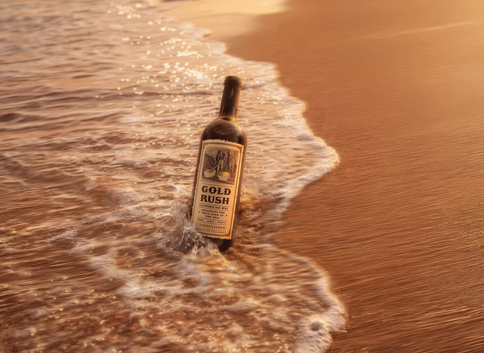 Wine bottle labeled GOLD RUSH half-buried in surf on a sunlit sandy beach