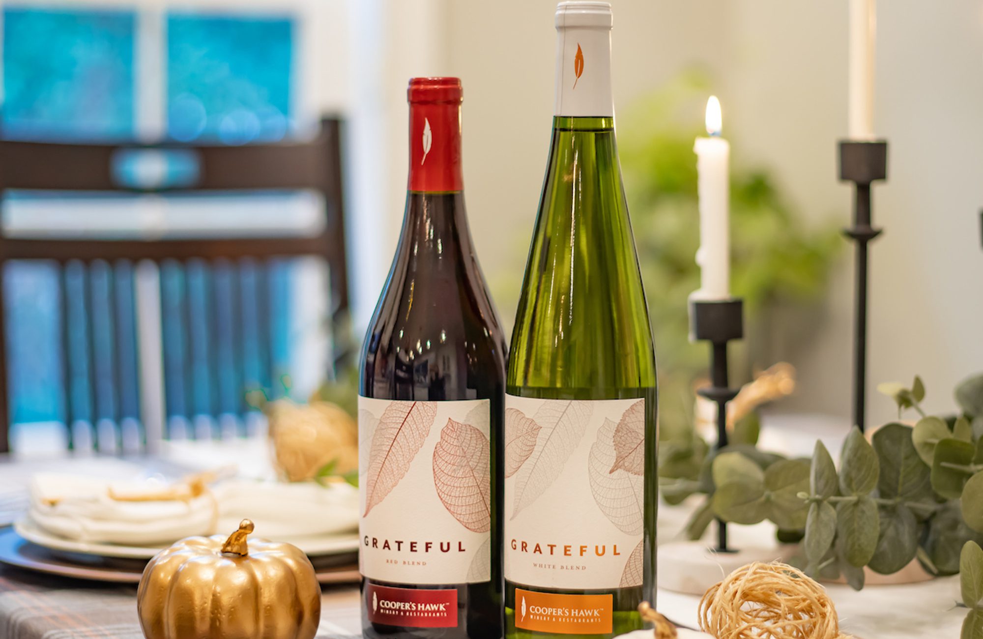 Two bottles of wine sit on a table next to pumpkins.