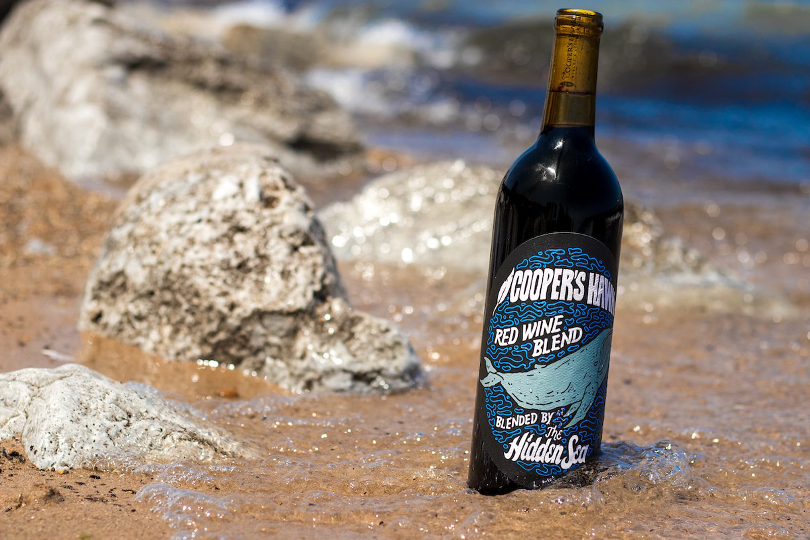 A bottle of wine sitting in the sand.