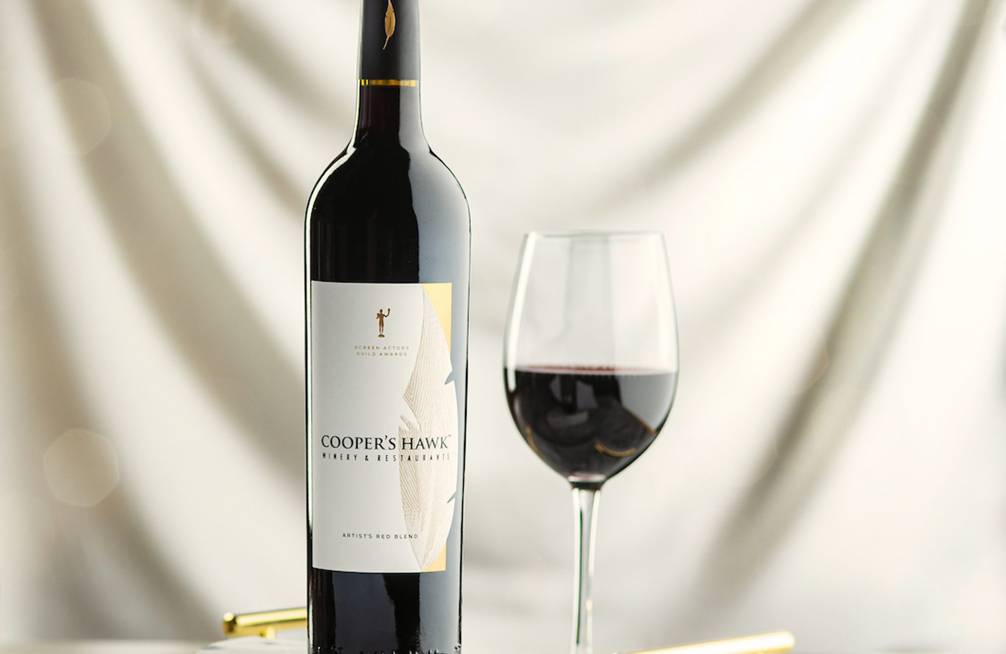 A bottle of red wine and a glass on a marble table.