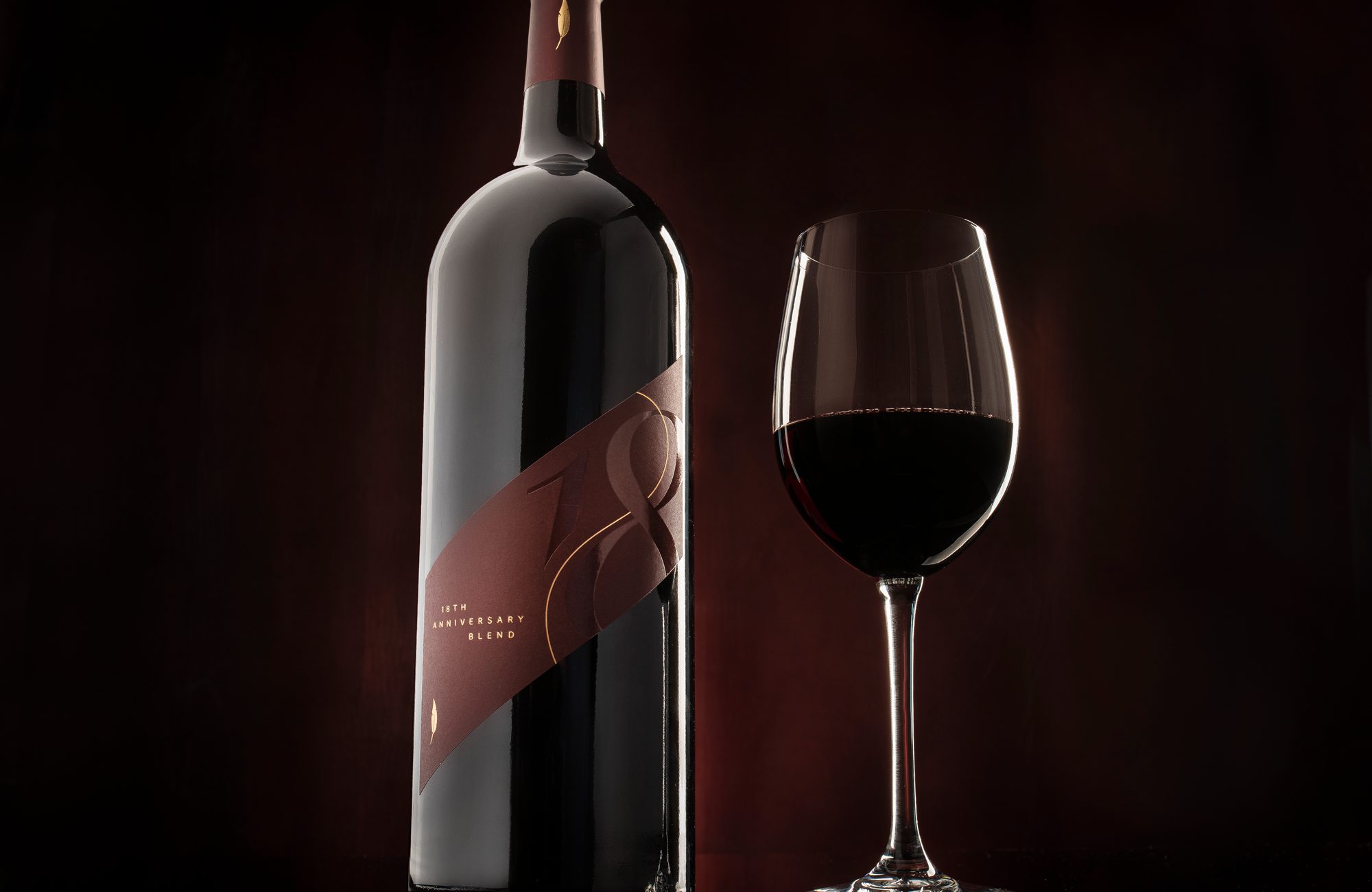 A bottle of wine and a glass on a dark background.
