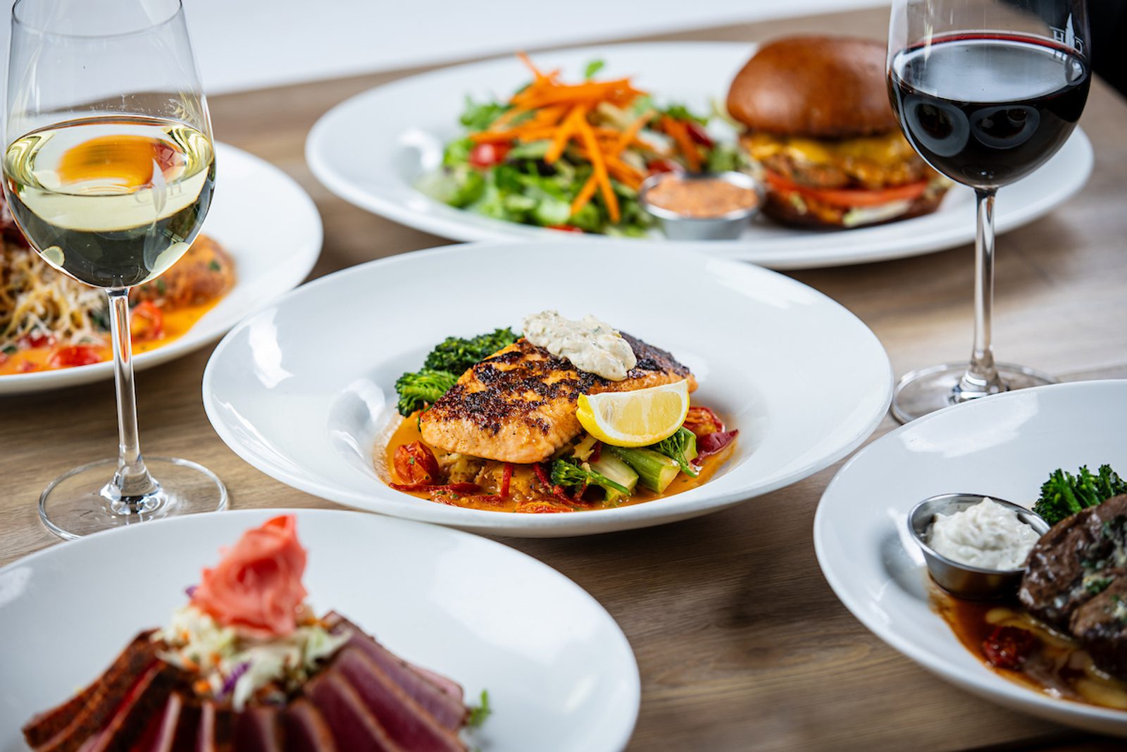 Grilled salmon fillet with herb butter and lemon wedge on vegetables in tomato sauce, red and white wine glasses