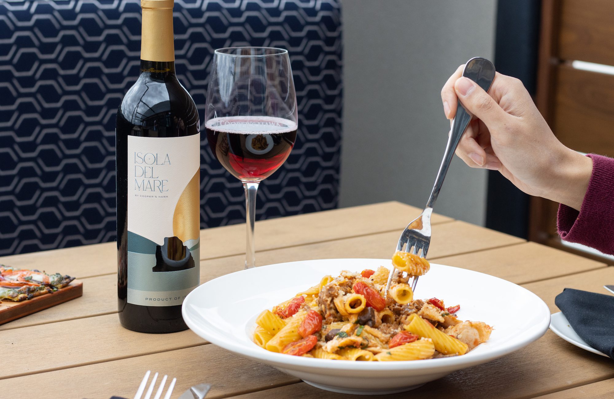 A person eating pasta with a fork next to a bottle of wine.