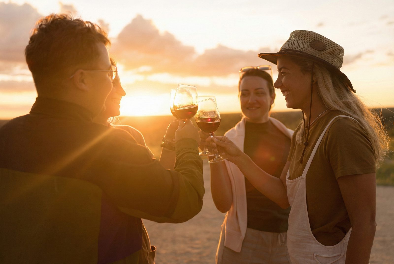 Four people toasting with red-wine glasses outdoors at sunset