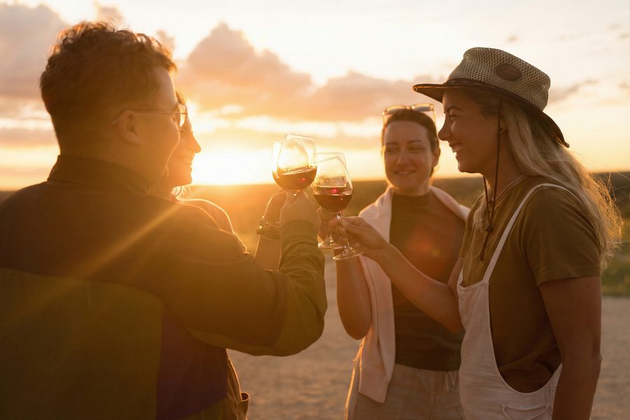 Four people toasting with red-wine glasses outdoors at sunset