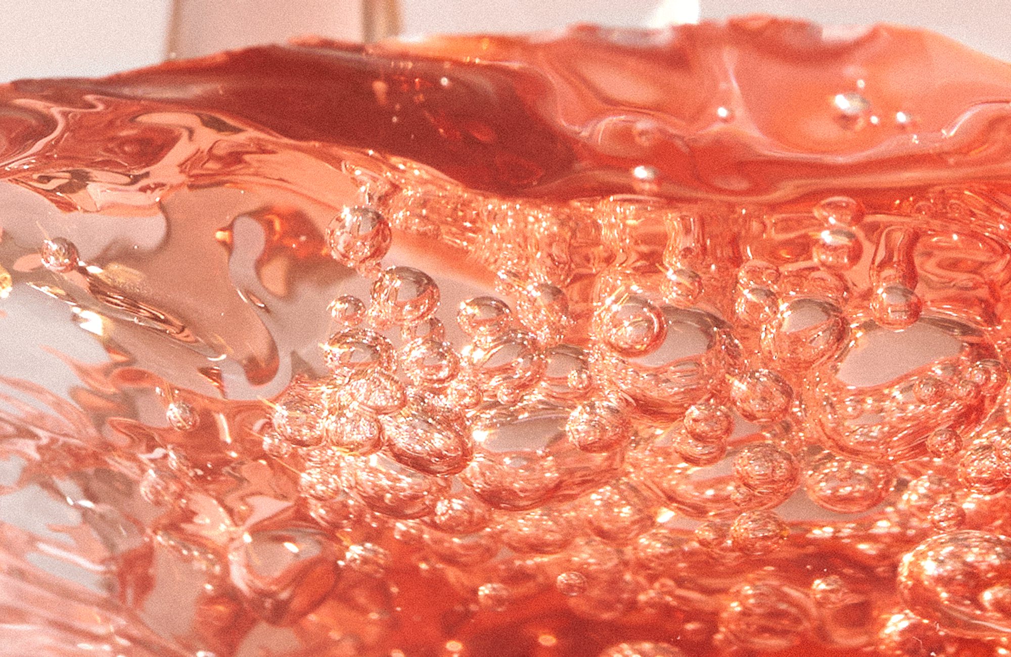 Translucent pink-orange liquid with clustered bubbles and a rippling surface