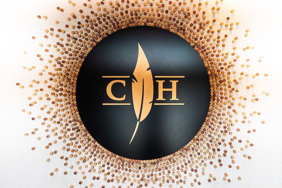 Black circular logo with gold feather and text "C H" between horizontal lines, surrounded by radiating gold studs