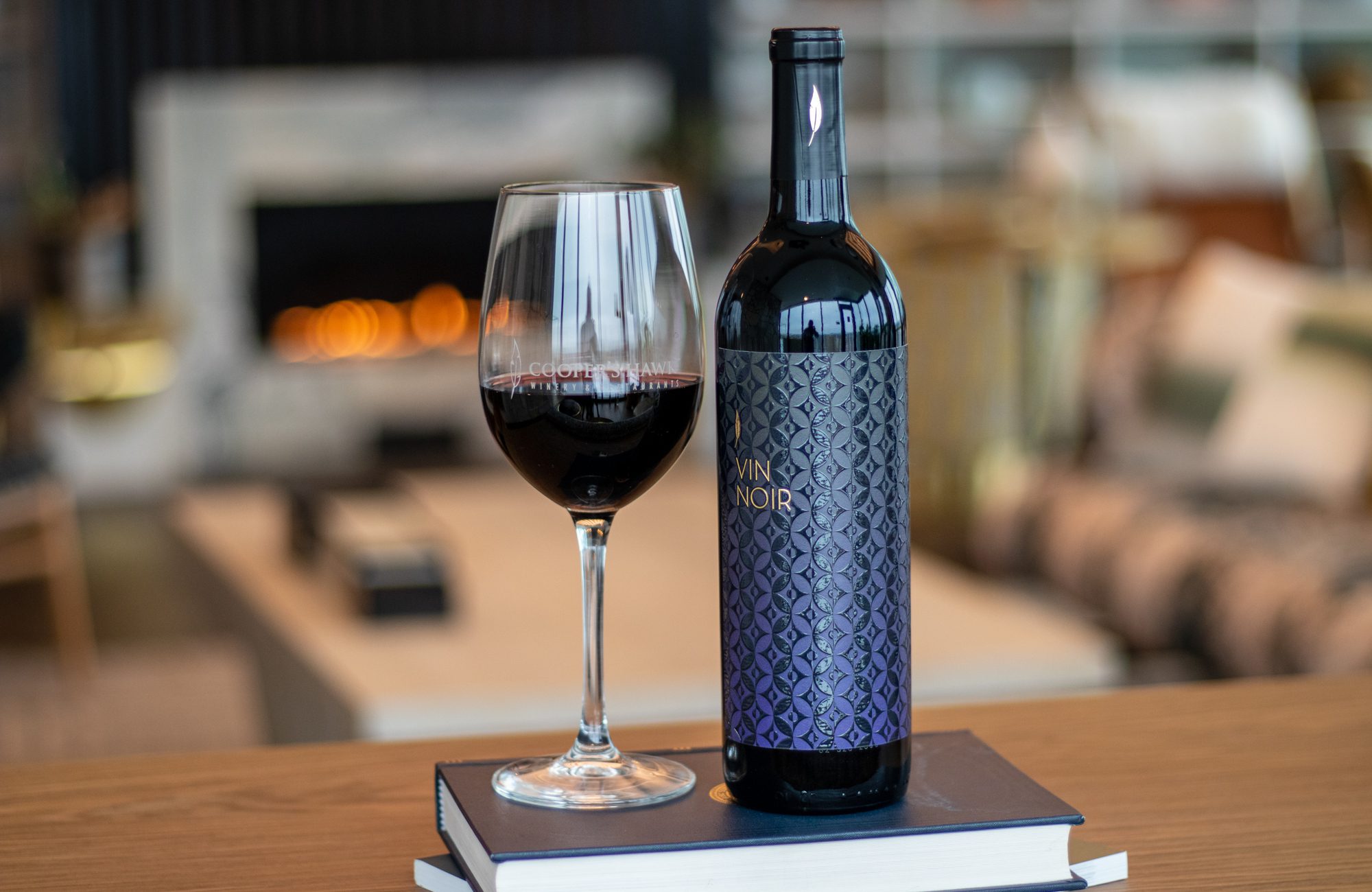 A bottle of wine sits on a table next to a fireplace.