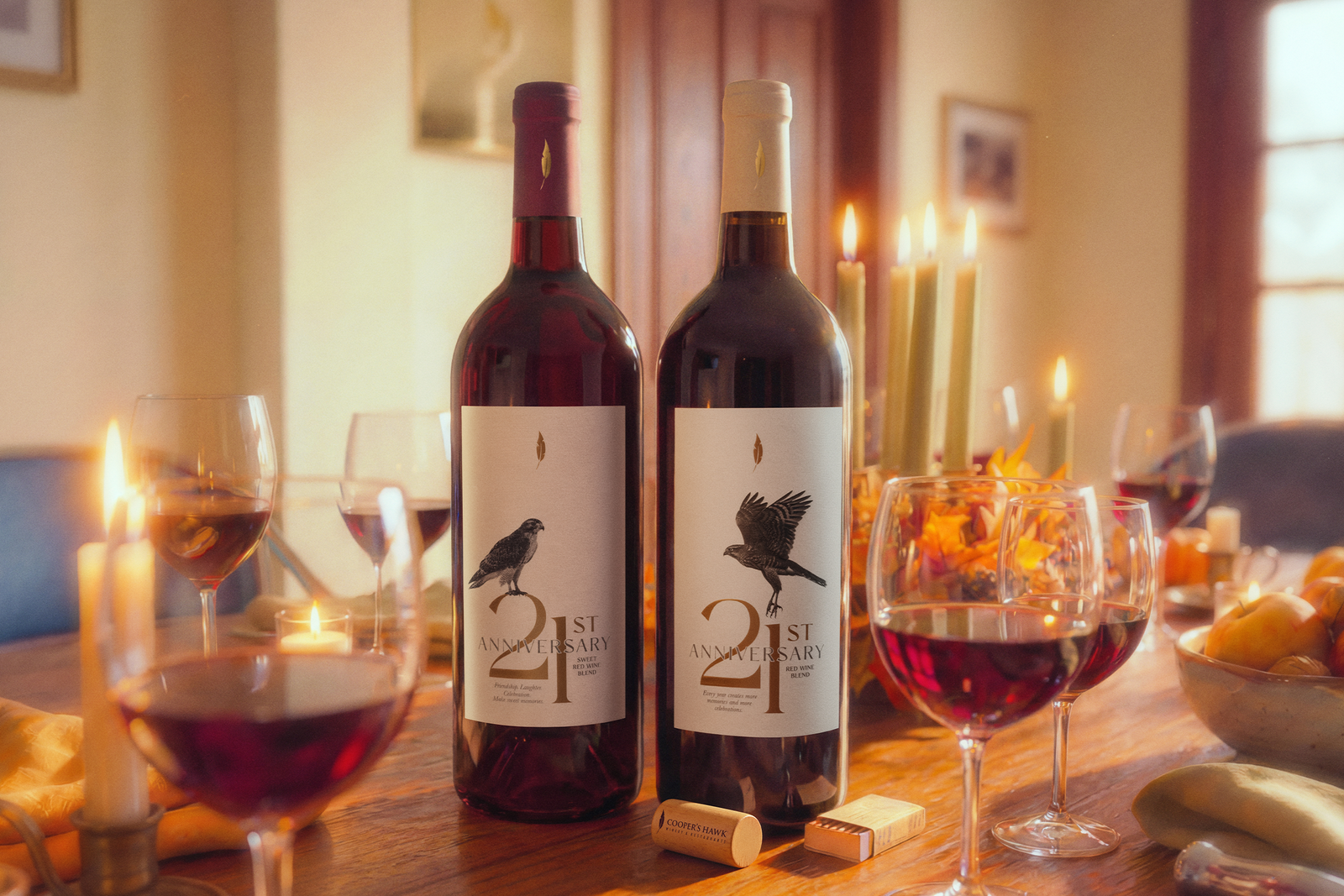 Two red wine bottles labeled “21st Anniversary” on a candlelit dinner table with wine glasses, candles, and autumn decor in a warm, cozy room