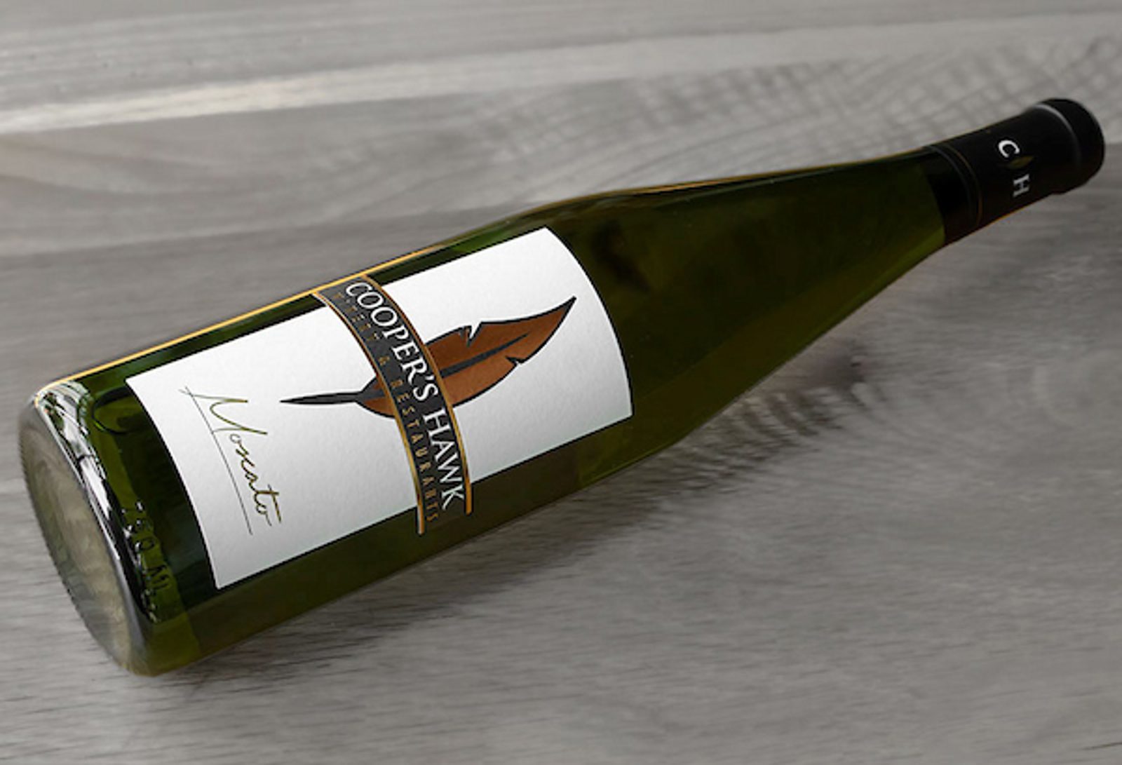Green Cooper's Hawk wine bottle lying on a wooden surface; label with feather logo and text COOPER'S HAWK and Veneto