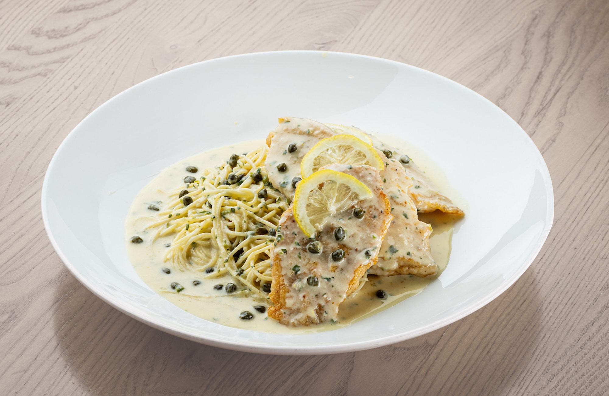 Breaded chicken cutlets topped with creamy lemon-caper sauce and lemon slices, served with spaghetti