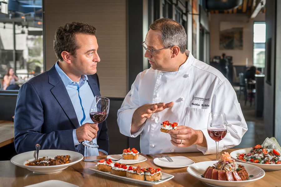 Two men talking at a table with plates of food.
