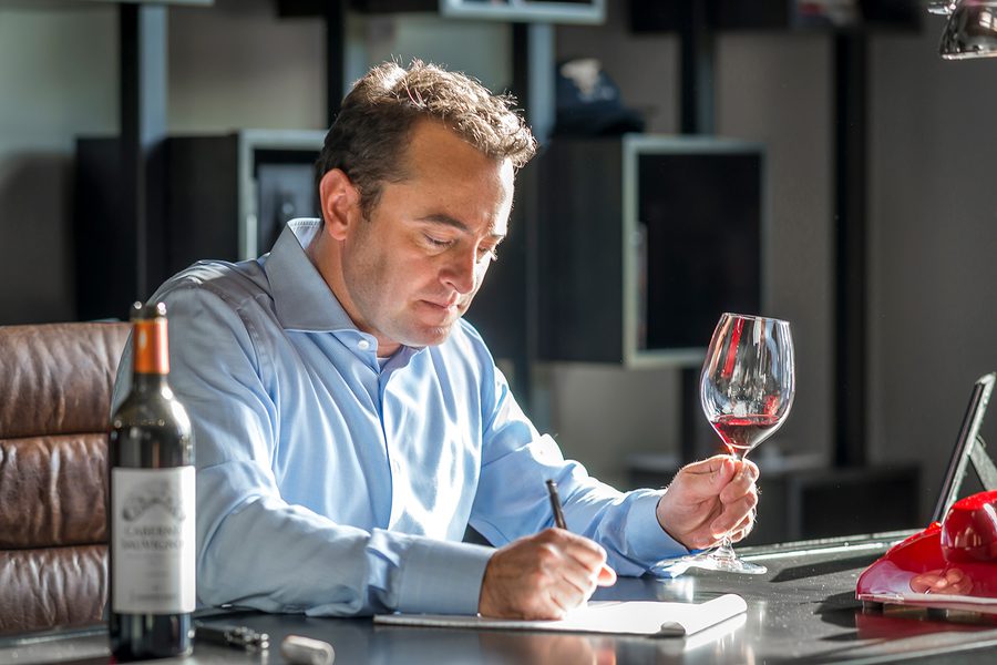 A man writing in a notebook while holding a glass of wine.