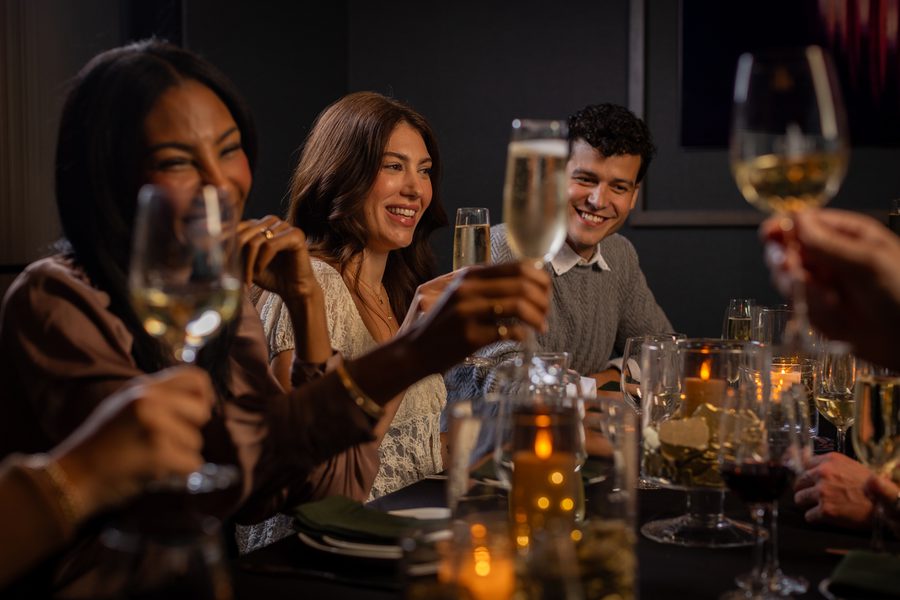 Friends smiling and toasting with champagne glasses at a candlelit dinner table in a dim restaurant