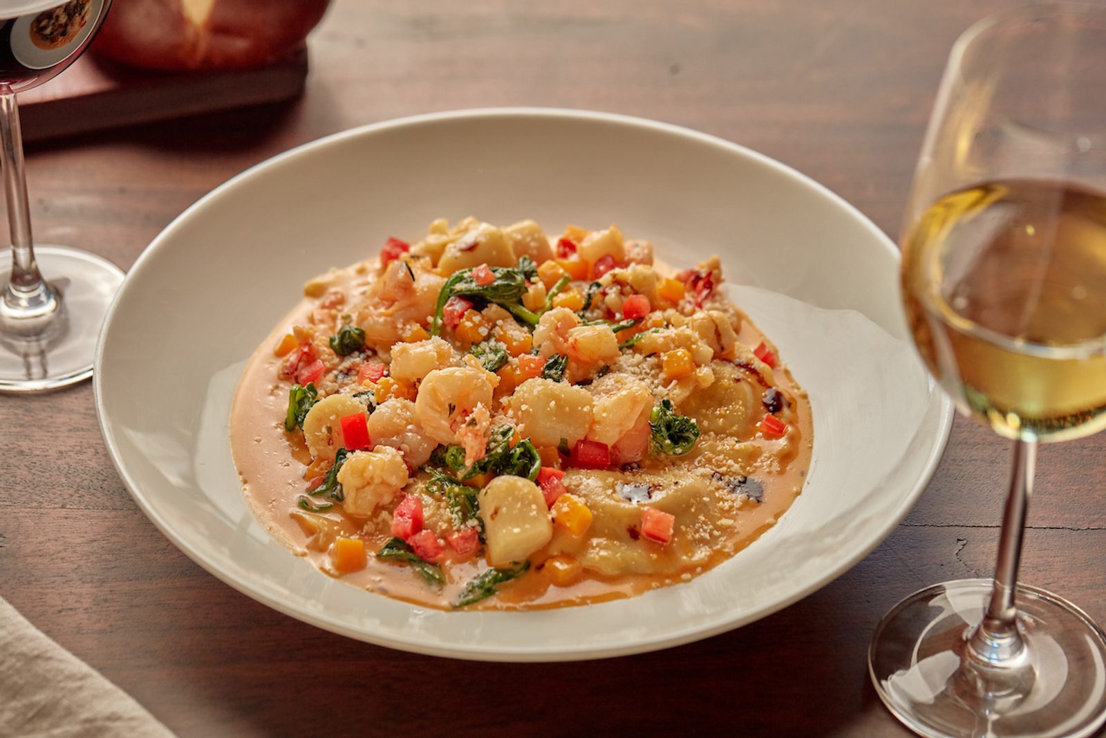 Plate of gnocchi in creamy vegetable sauce with herbs and grated cheese, served on a wooden table beside two glasses of white wine