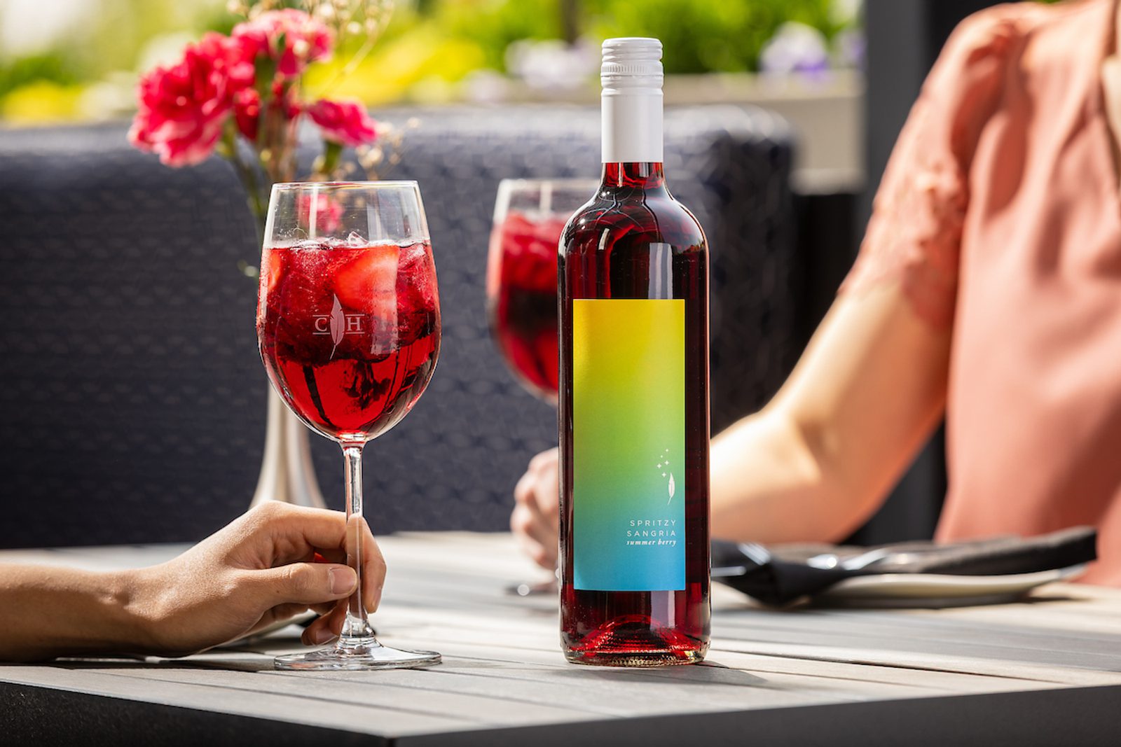 Summer Berry Spritzy Sangria Bottle Image with glasses of the wine in the background with people