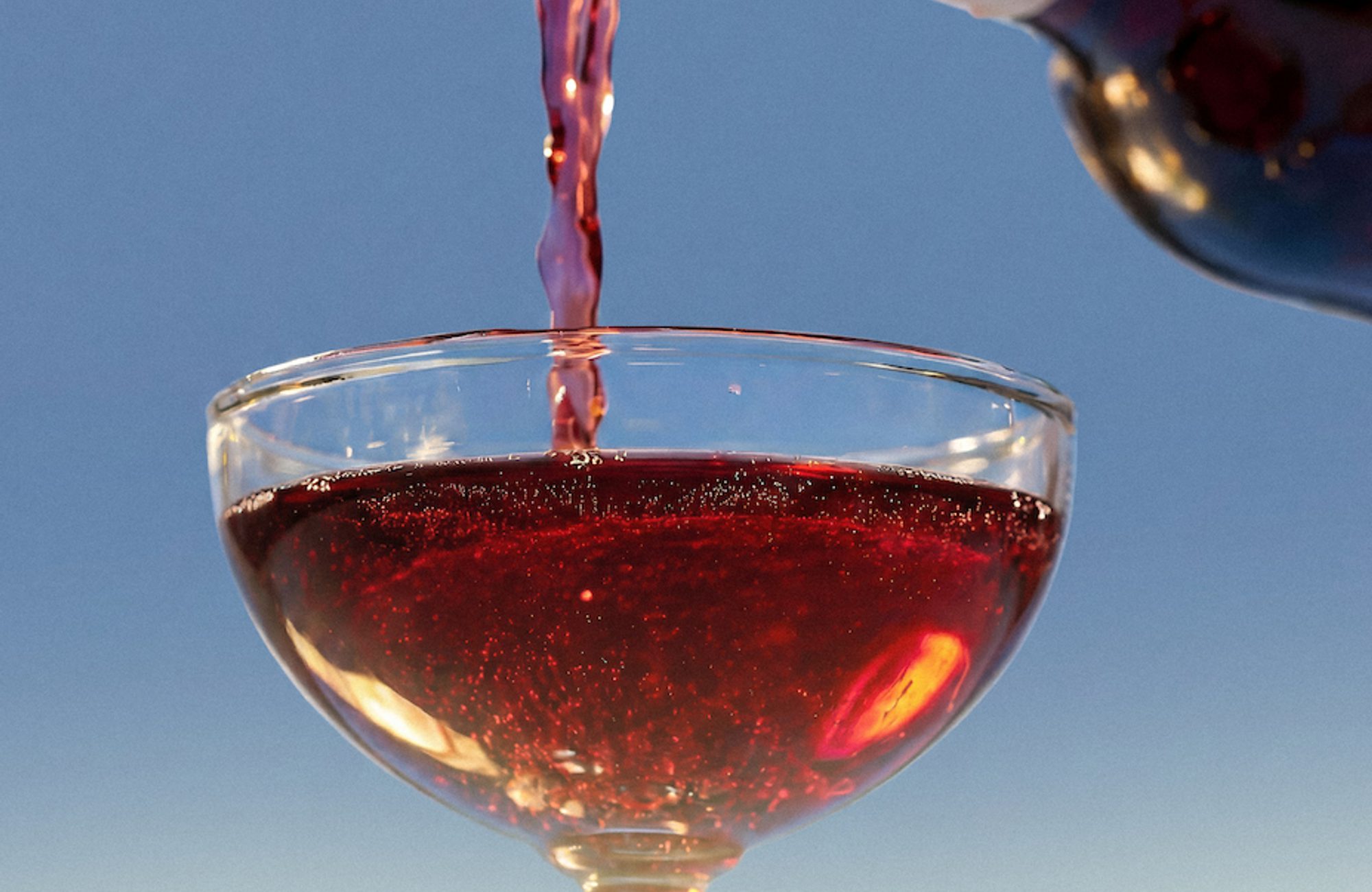 Red wine being poured from a bottle into a shallow coupe glass