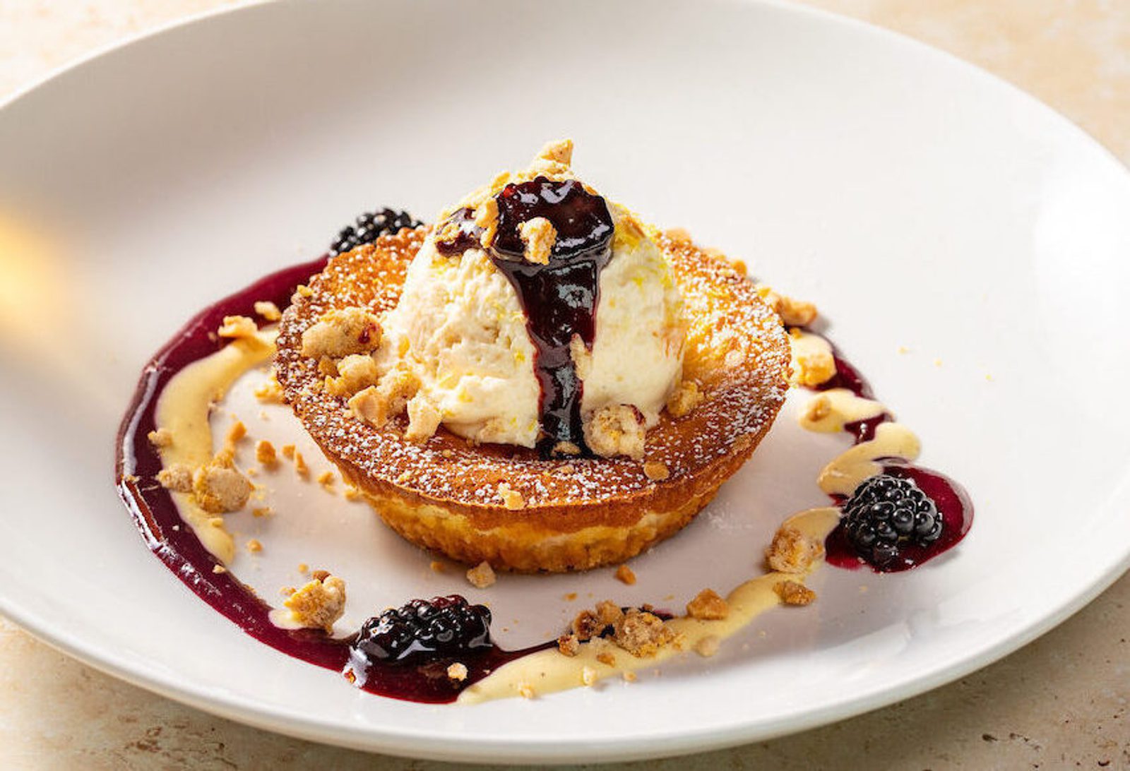 Tart topped with vanilla ice cream, drizzled berry sauce, blackberries and crumbled nut garnish.