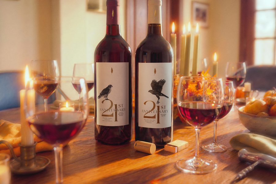 Two labeled wine bottles on a candlelit table with several filled wine glasses, fruit, corks, and warm sunlight streaming through a dining room.