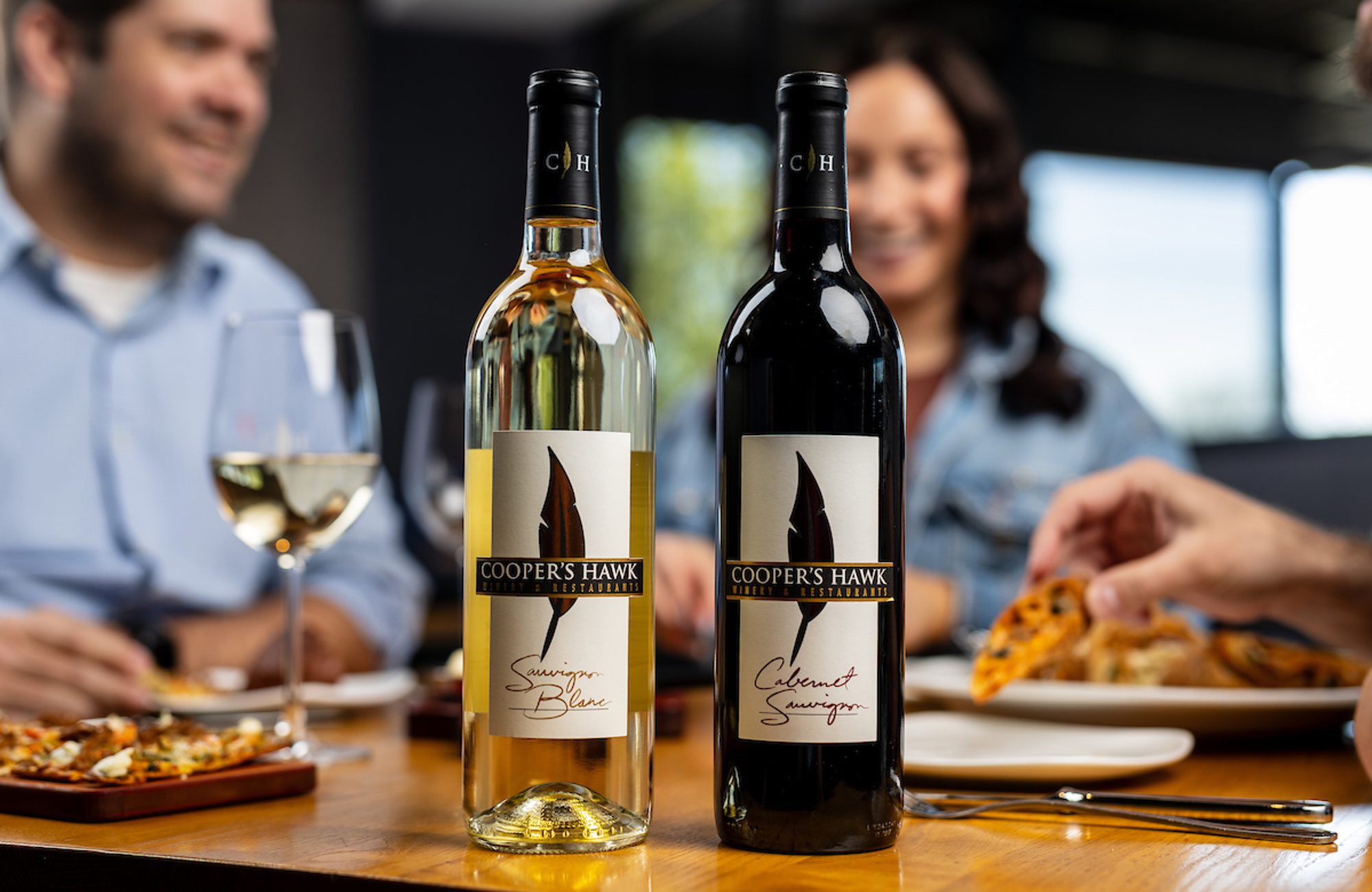 Image of people dining with cooper's hawk red and white wine bottles in front of them
