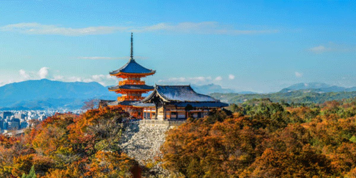 Temple with pagoda atop a forested hill in autumn, city below and distant mountains on the horizon
