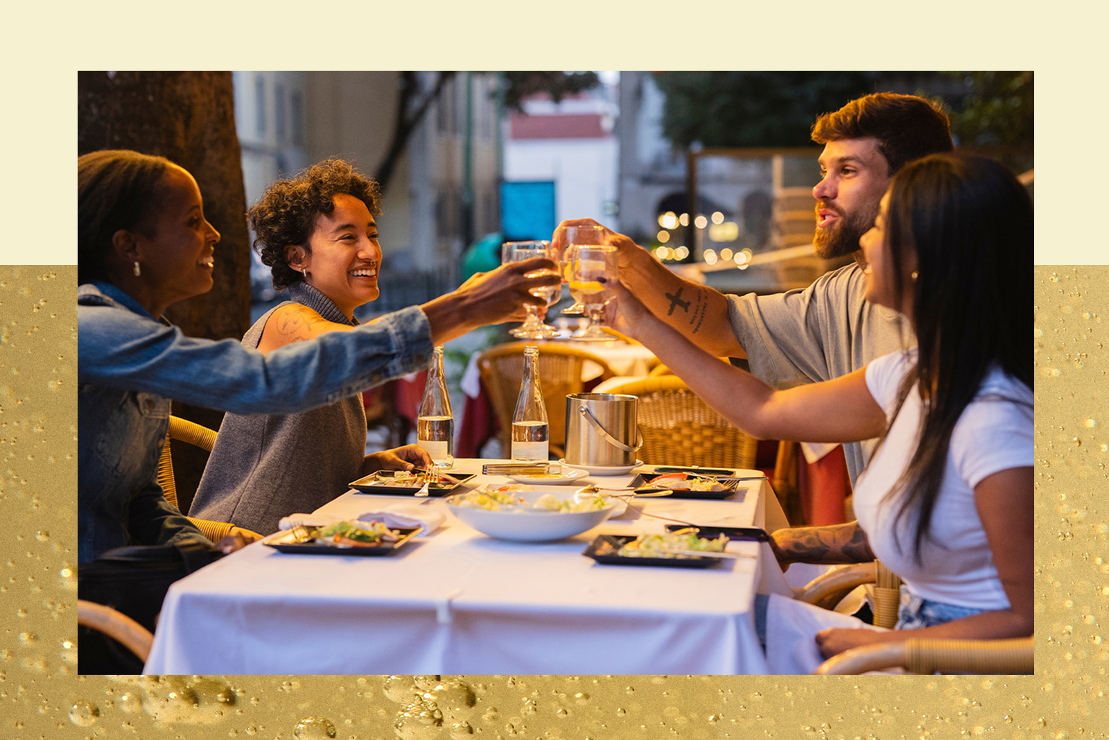 Four friends toasting with wine glasses at an outdoor restaurant table during dinner