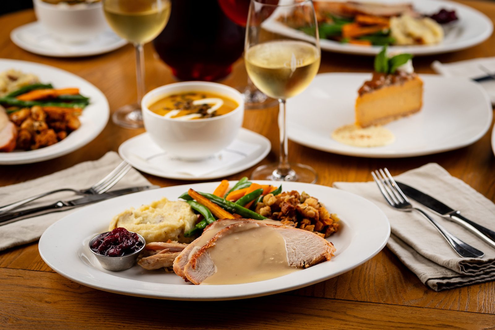 Sliced turkey with gravy, mashed potatoes, green beans, carrots, stuffing and cranberry sauce; wine and soup behind.