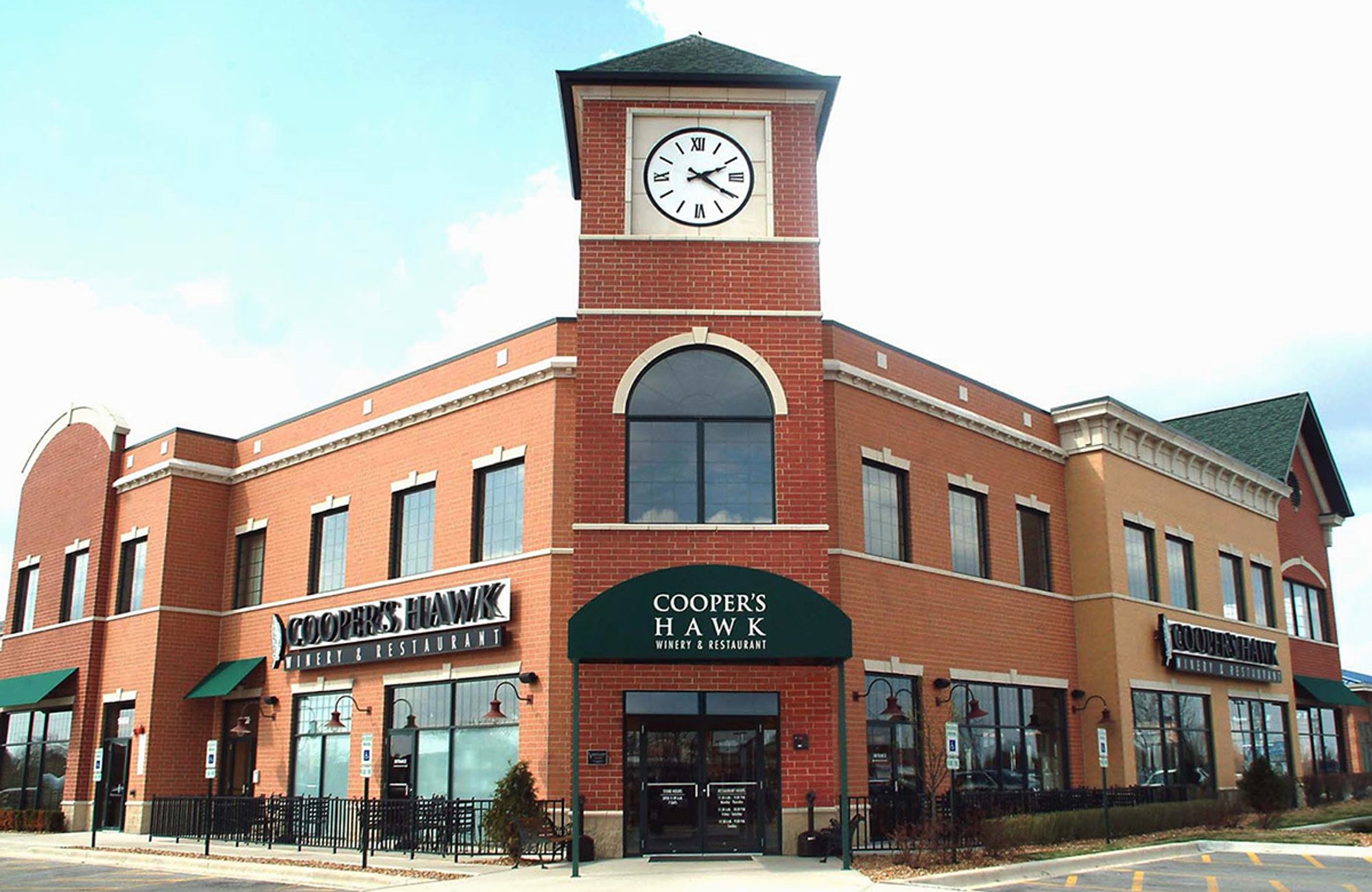 Brick Cooper’s Hawk Winery & Restaurant building with a central clock tower, large arched windows, and green awnings under a bright sky